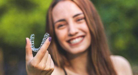 Woman happily showing off her Invisalign tray while living life